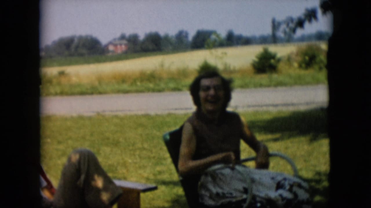 Woman seated in a lawn chair smiling in a shaded grassy yard.