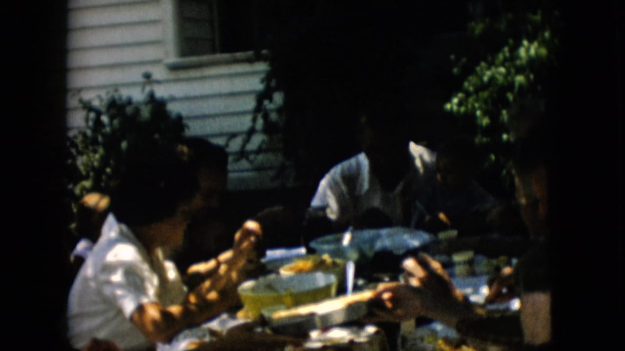 Family members seated at an outdoor table with dishes and bowls in shade.