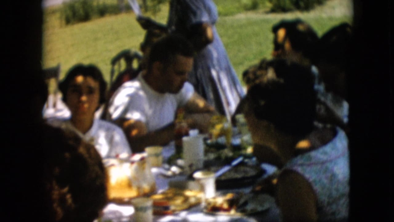 Group of adults eating at a picnic table beside a swing set.
