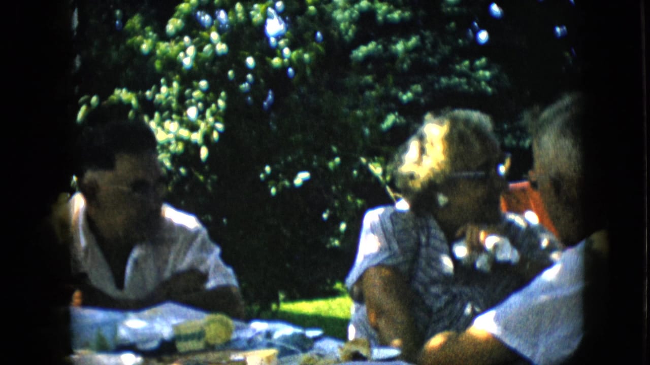 Woman in glasses turns while seated with two men at an outdoor table.