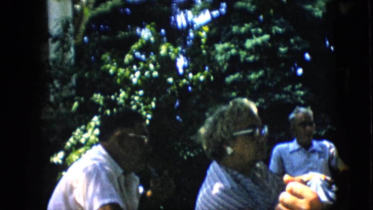 Three adults seated outdoors, including an older woman and a man in glasses.