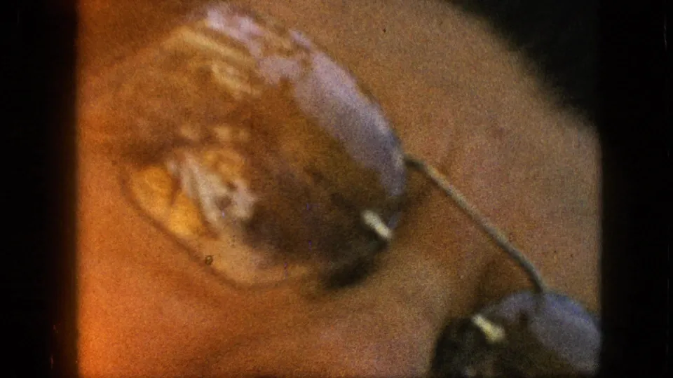 A tight, soft-focus home-movie close-up shows food held near the lens, with warm color cast, grain, and film-edge flare.