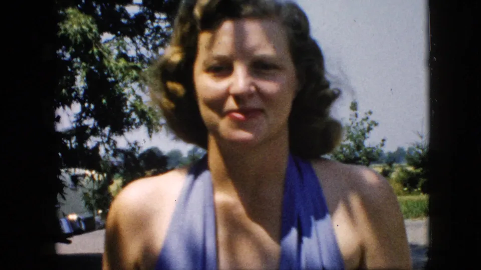 Close, soft-focus view of an adult woman in a blue halter swimsuit looking toward the camera in 1957 United States home-movie footage.
