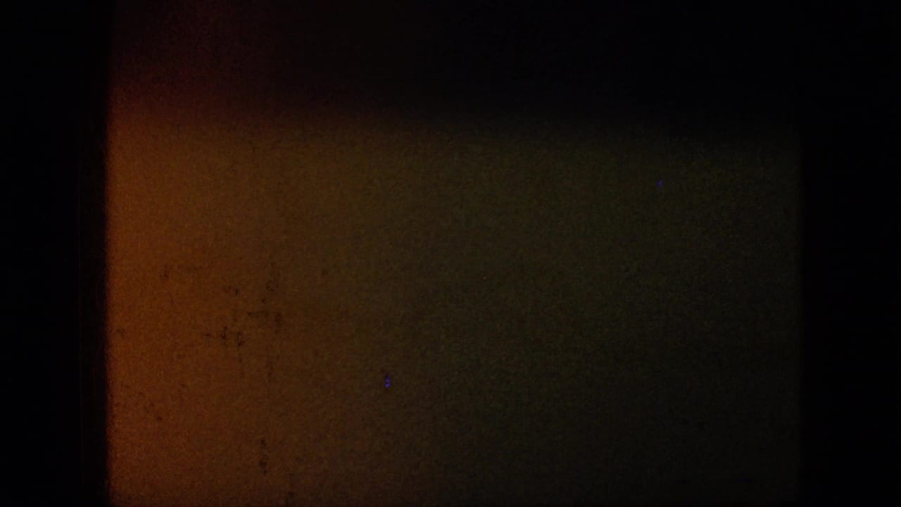Dark 1957 8mm home-movie frame from the United States reel, showing heavy grain, black borders, and a faint warm exposure area without identifiable people or places.