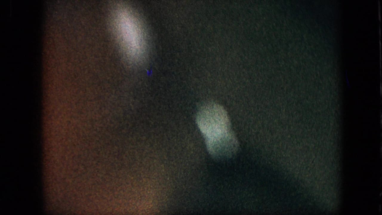 Grainy 1957 8mm home-movie frame with green and brown color cast, soft pale light flares, and no clearly identifiable subject in the visible still.