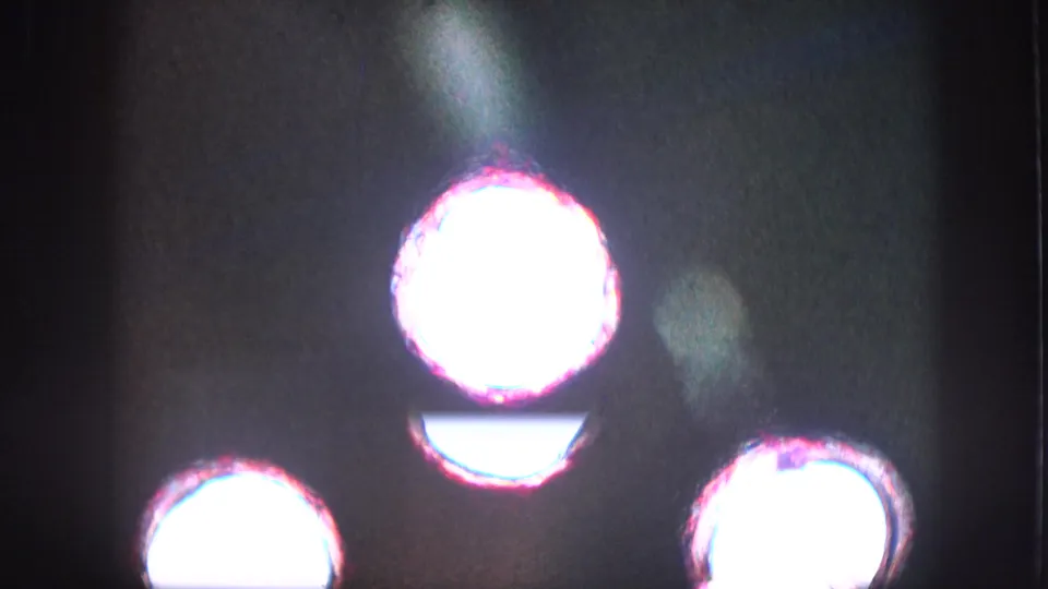 Overexposed 8mm home-movie frame from the 1957 United States reel, with bright circular light forms, magenta fringing, grain, and dark surrounding exposure.