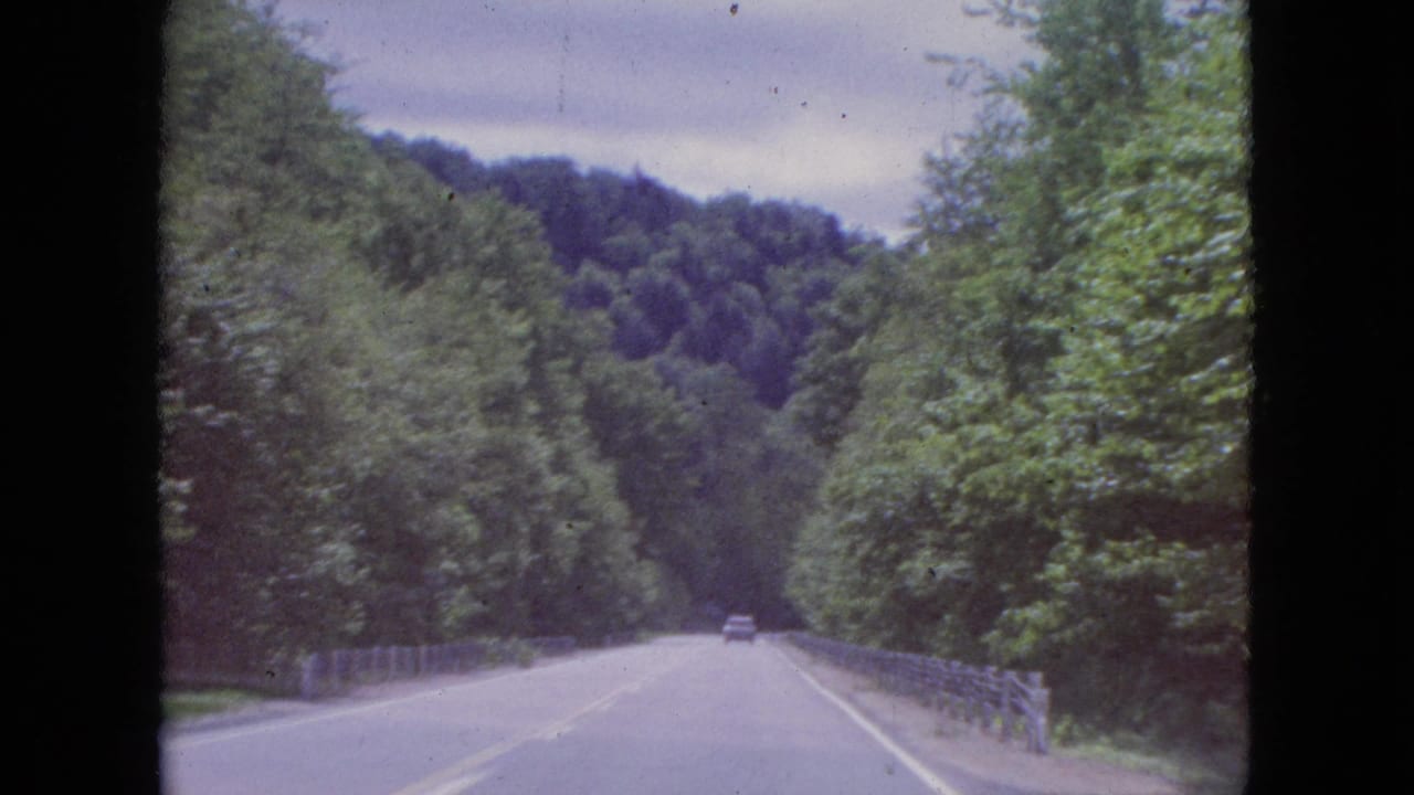 Roadway crossing a guarded stretch with trees and hills in the distance.