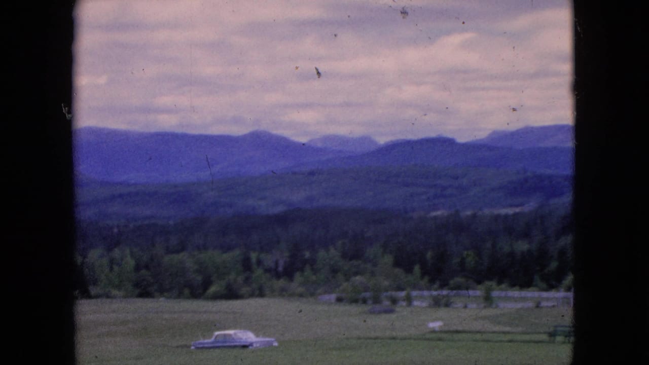 Distant mountains and forested valley with a white car near the lower field.