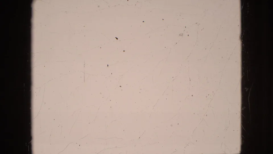 End frame from the 8mm scan showing little scene detail, with pale exposure, film scratches, dust specks, and dark gate borders visible.