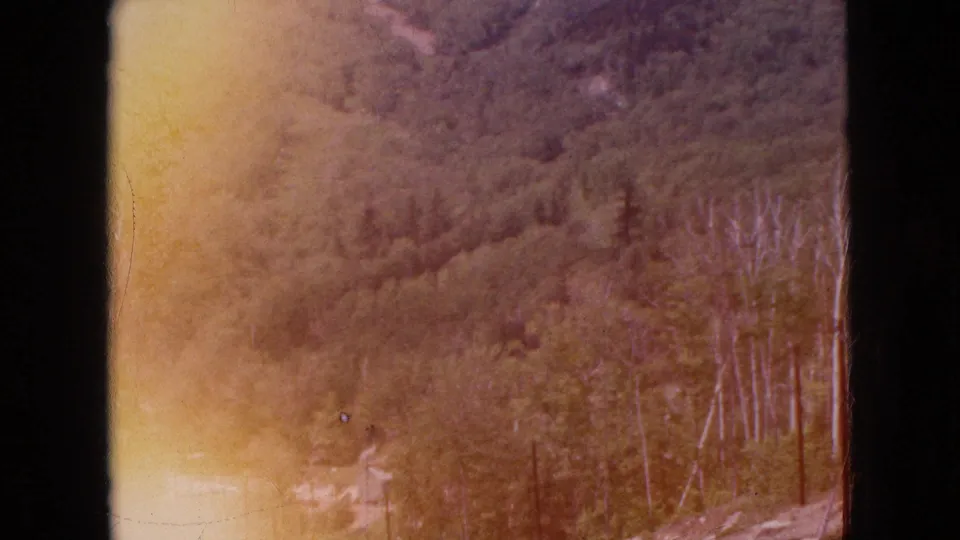 Color-shifted 8mm frame of the same mountain valley, where orange-red fading and warm exposure obscure parts of the forested hillside.