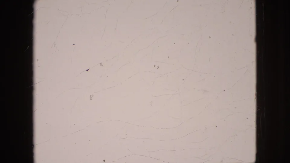 A mostly blank overexposed 8mm frame from the 1964 clip, with visible film scratches, dust, and dark vertical frame borders.