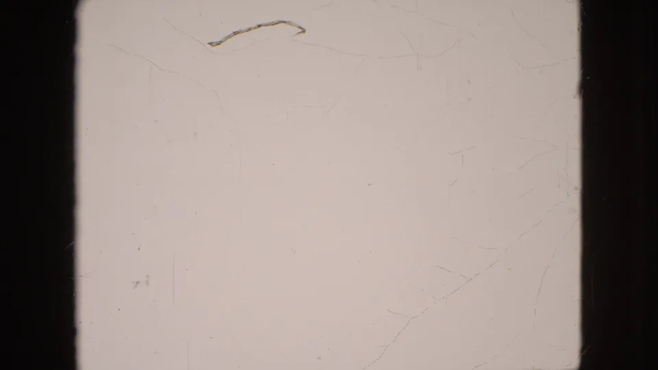 A pale 8mm frame with little visible scene detail, showing dark frame borders, scratches, and aged-film texture.