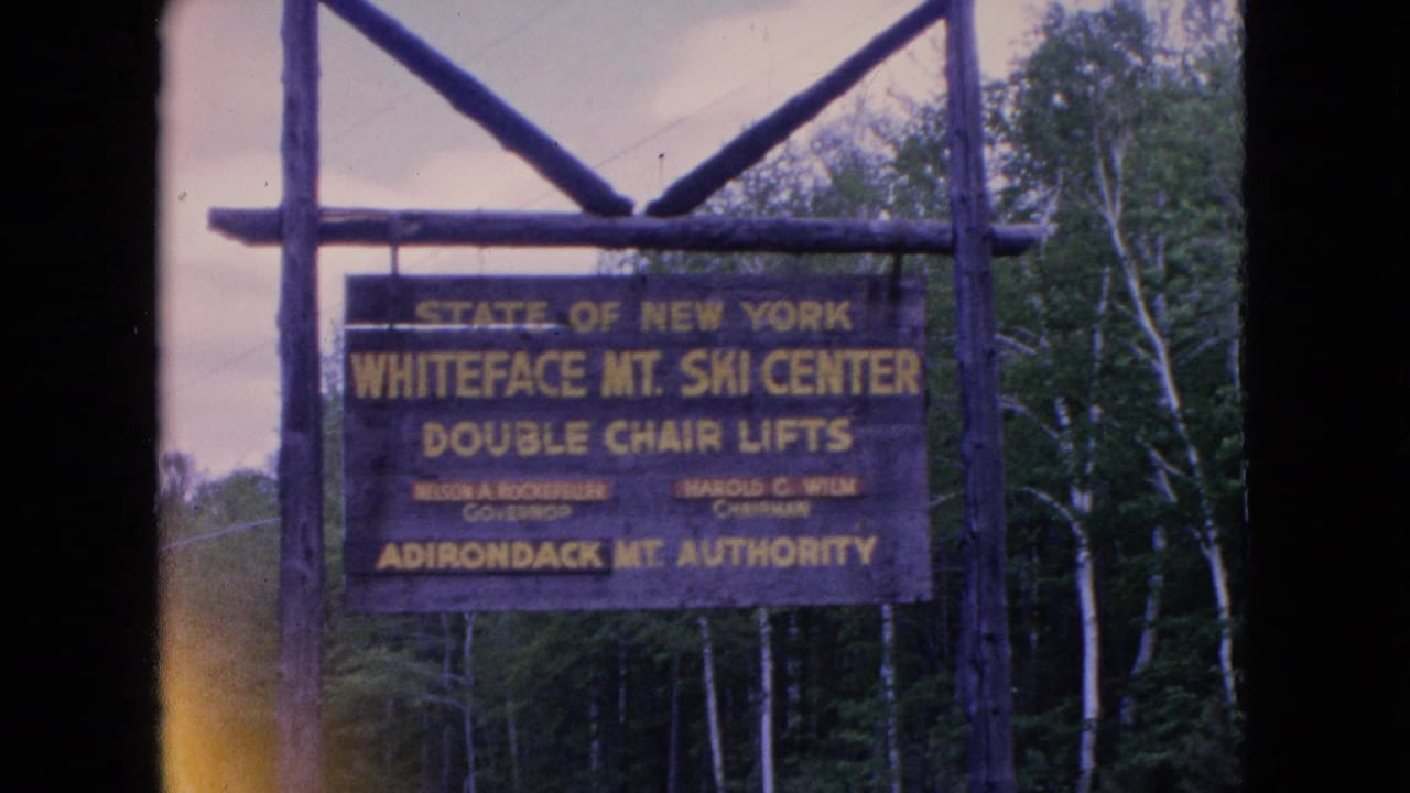 1964 8mm frame showing a wooden Whiteface Mountain Ski Center sign for double chair lifts mounted on rustic posts in a wooded New York mountain setting.