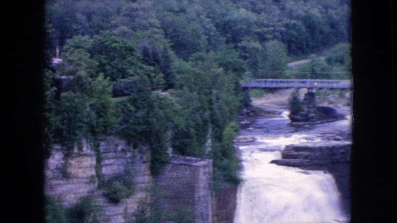 Bridge over rushing river water with forest and stone walls nearby.