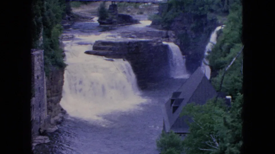 The final frame holds on the tiered river drop in the Niagara Falls, New York area, with a bridge above the rapids, trees on both sides, and a steep roof at lower right.