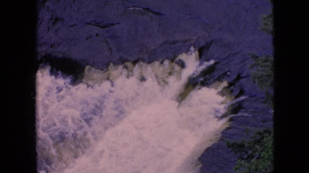1964 8mm home-movie frame of Niagara Falls in New York showing white water surging across a dark blue-purple surface with soft film grain.