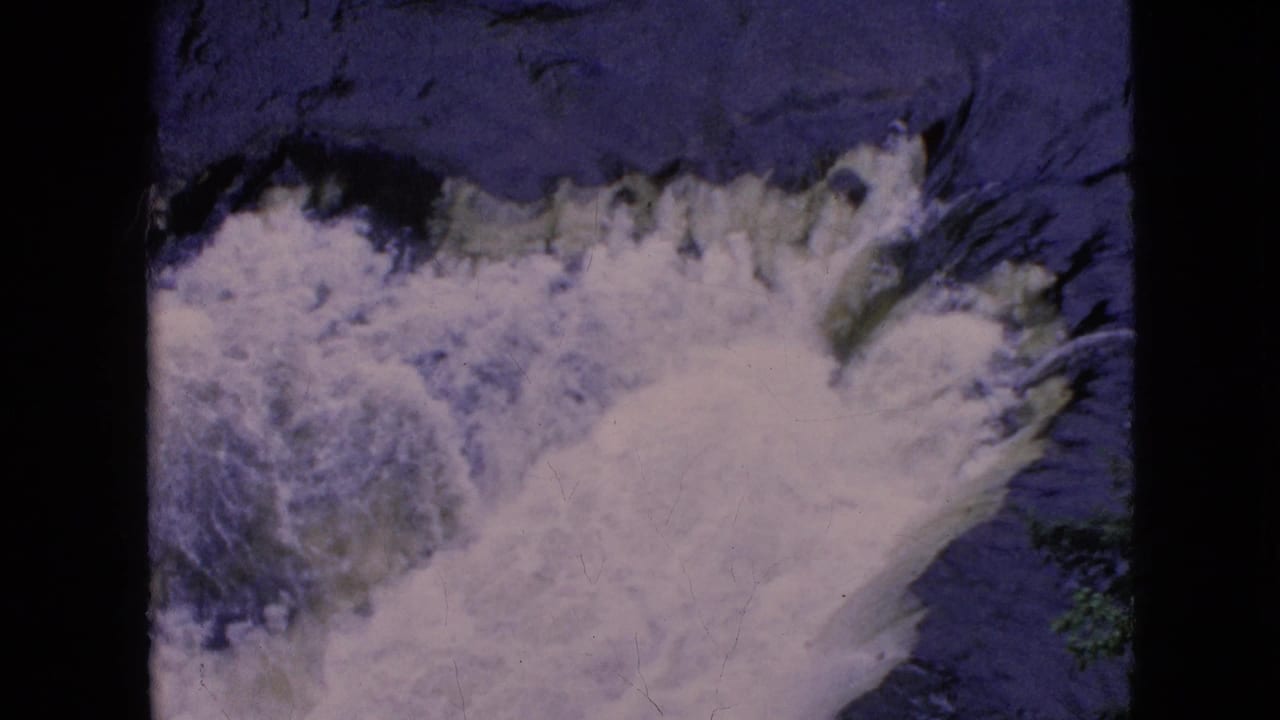 1964 8mm frame of Niagara Falls where the cascade spreads diagonally through dark, blue-purple water with visible small-gauge film texture.