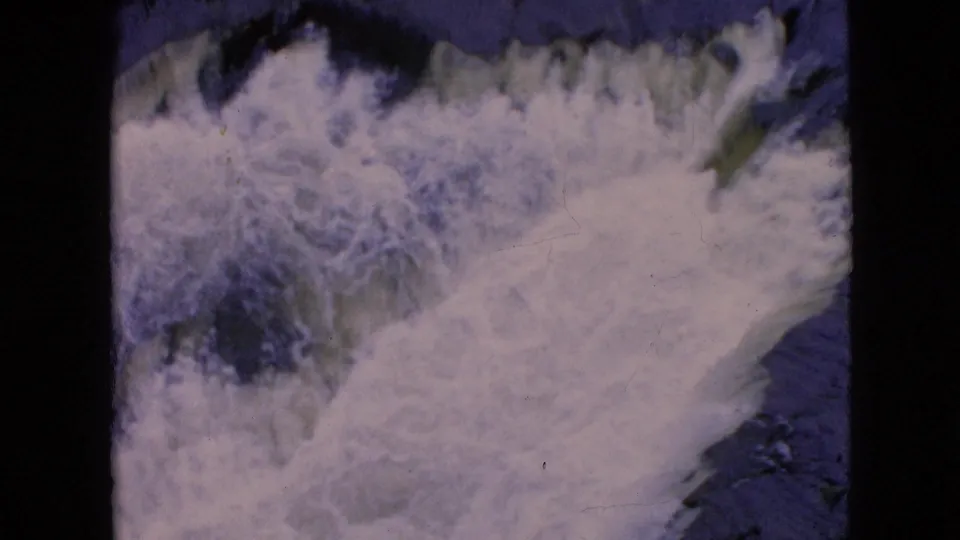 1964 8mm home-movie view of Niagara Falls with turbulent white water filling much of the frame and darker water visible along the edge.