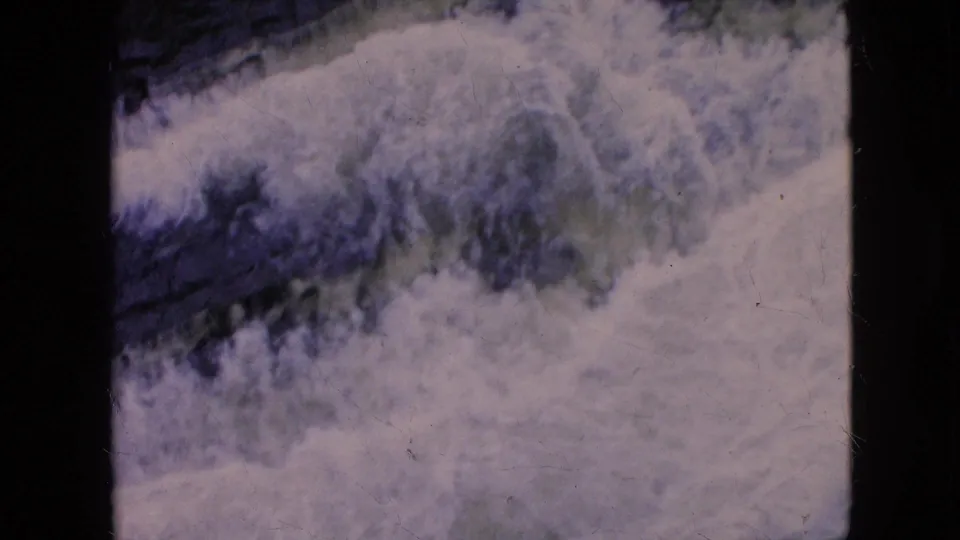 1964 8mm Niagara Falls, New York home-movie frame showing a broad area of foaming river water with shadowed blue-green channels.