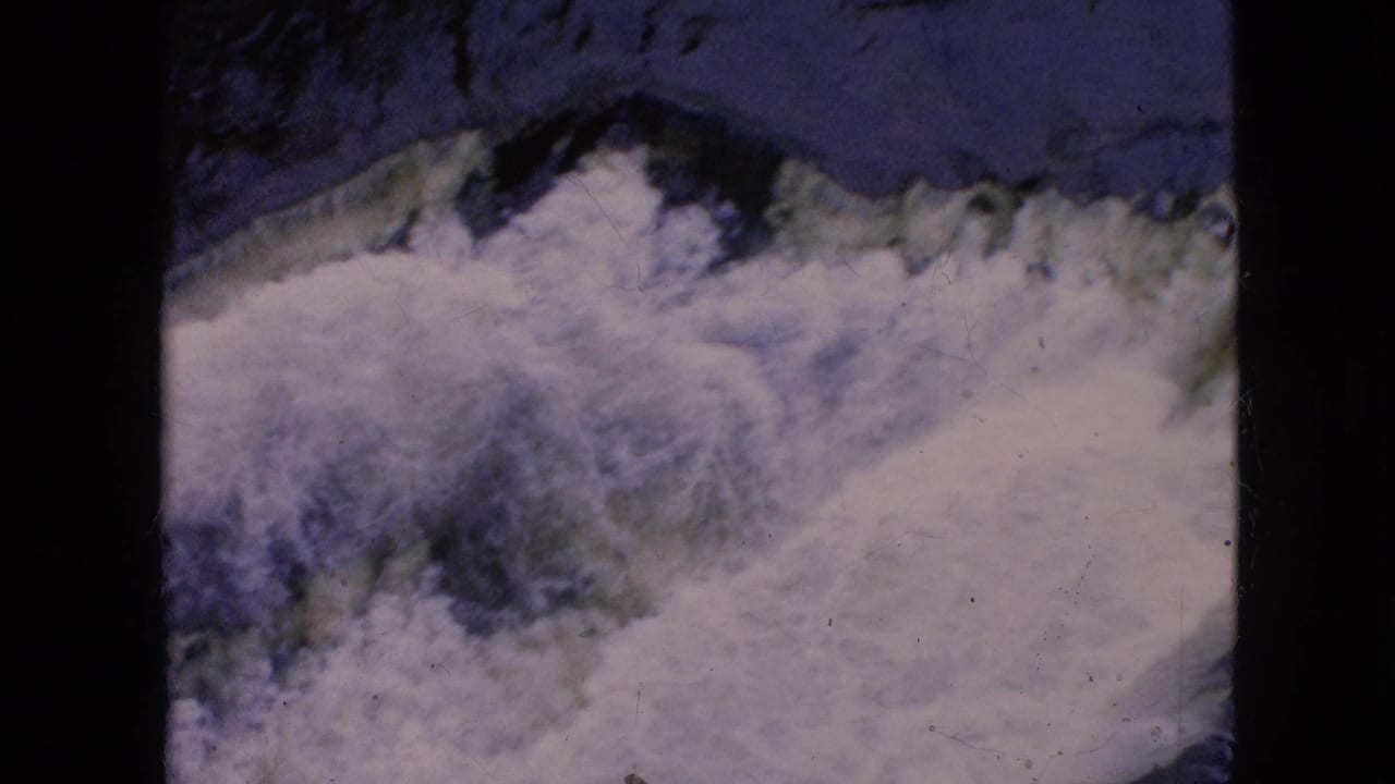 1964 8mm home-movie frame showing turbulent white water and dark rock at Niagara Falls, with soft focus, grain, scratches, and black film borders.