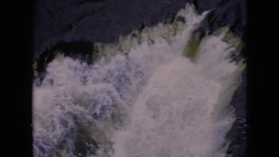 1964 8mm Niagara Falls footage showing frothy white water churning over dark rock, with the scanned film edge visible around the frame.