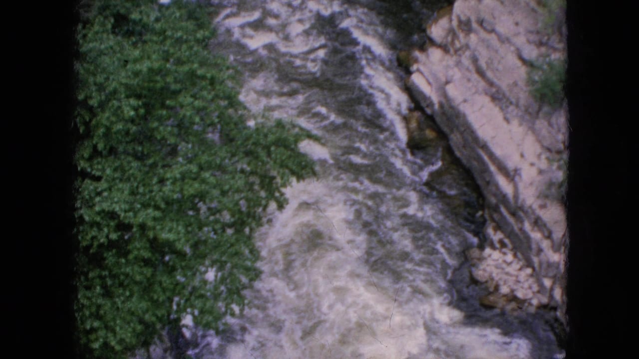 Fast river current bends through rock walls with leafy trees beside the water.