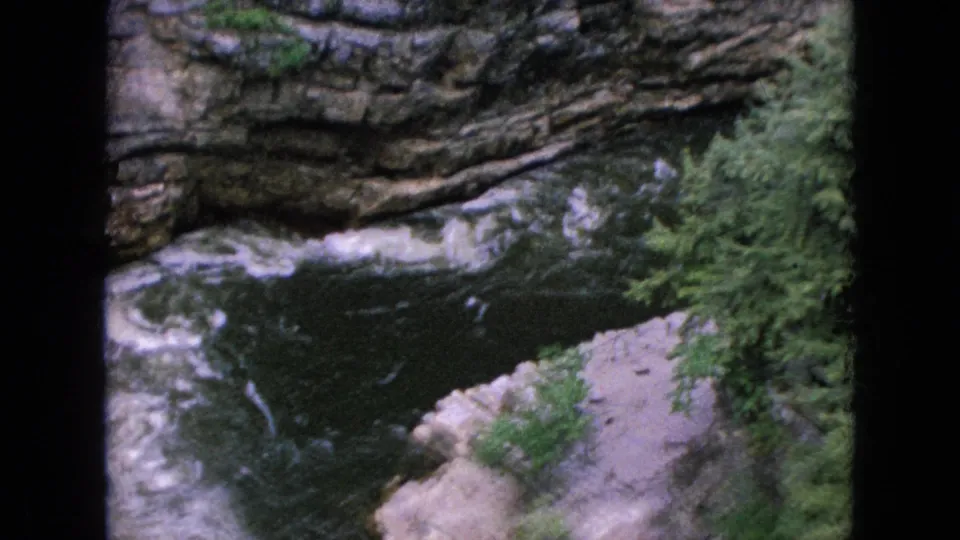 Vintage 8mm frame from the Niagara Falls, New York area showing a rocky gorge, fast-moving water, white foam, and dense green vegetation.