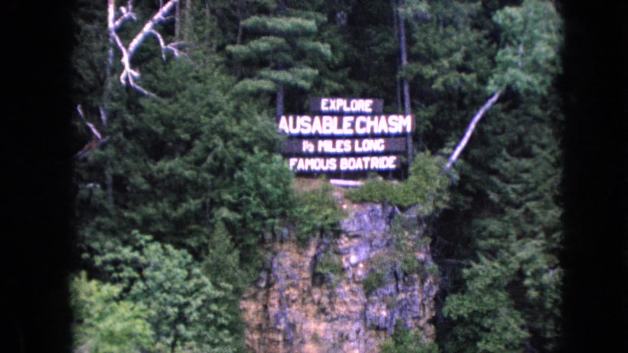 Tourist sign reading Ausable Chasm over a forested cliff face.