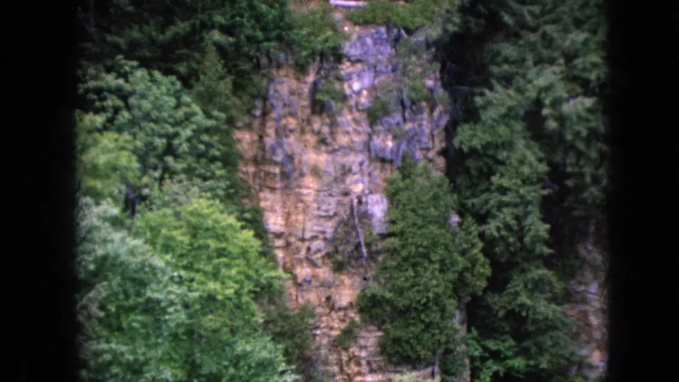 The frame widens or shifts to show more of the cliff and surrounding forest, with the Ausable Chasm sign partly near the top of the 8mm image.