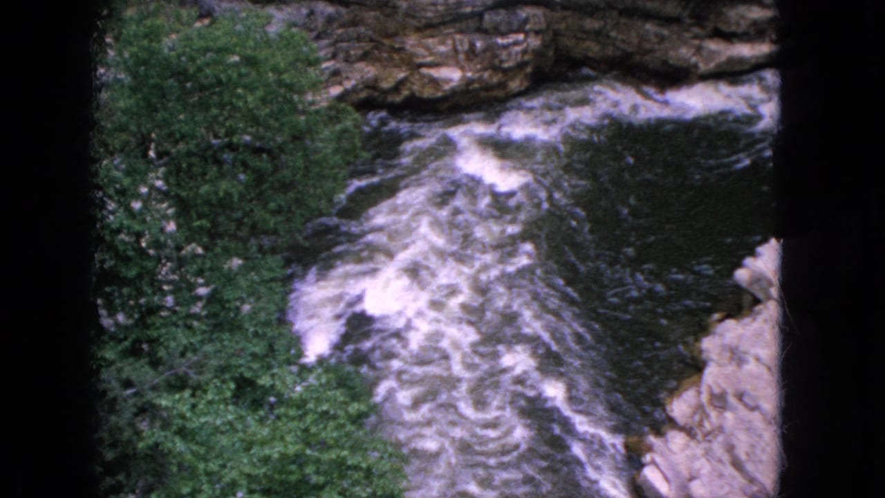 1964 Niagara Falls, New York home-movie frame showing turbulent white-water rapids in a rocky gorge, viewed from above with trees on the left side.