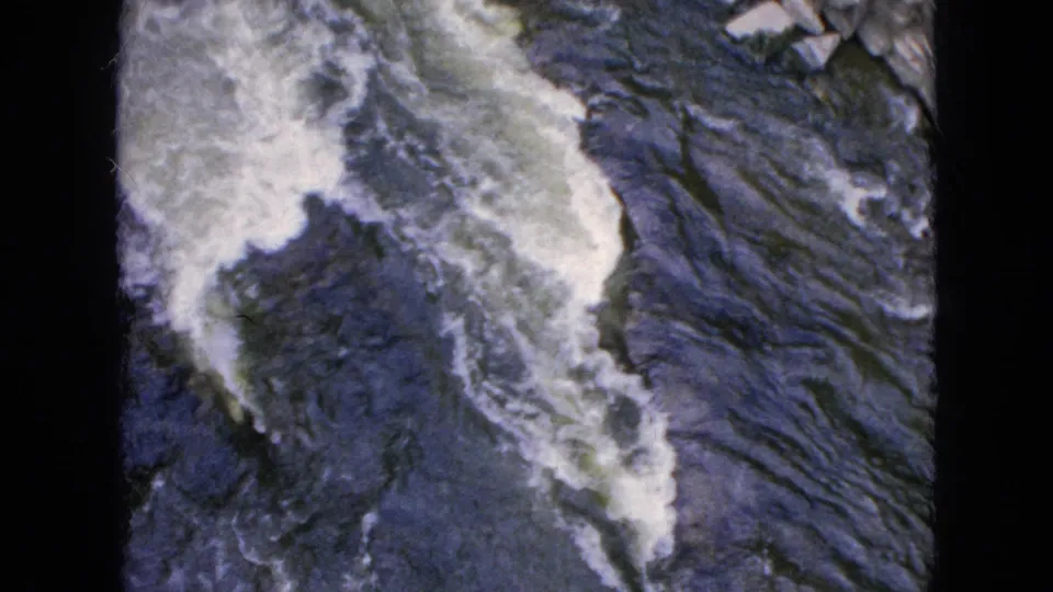 Foaming river water moves across dark rock at Niagara Falls in a grainy 1964 home-movie view.