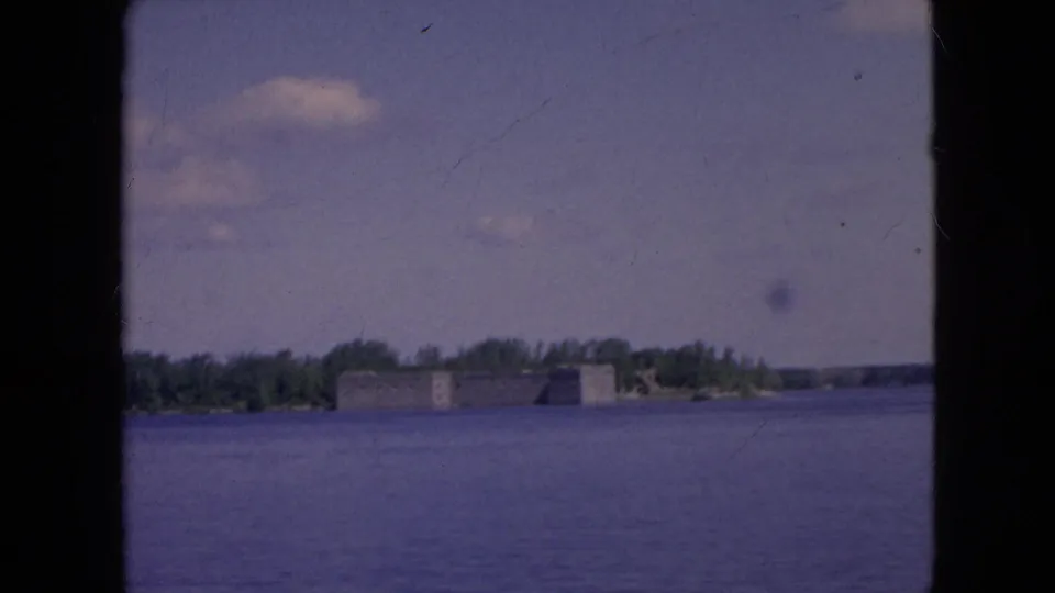 1964 8mm frame showing the river in the foreground and a low historic fort-like structure on the far shoreline near Niagara Falls, New York.
