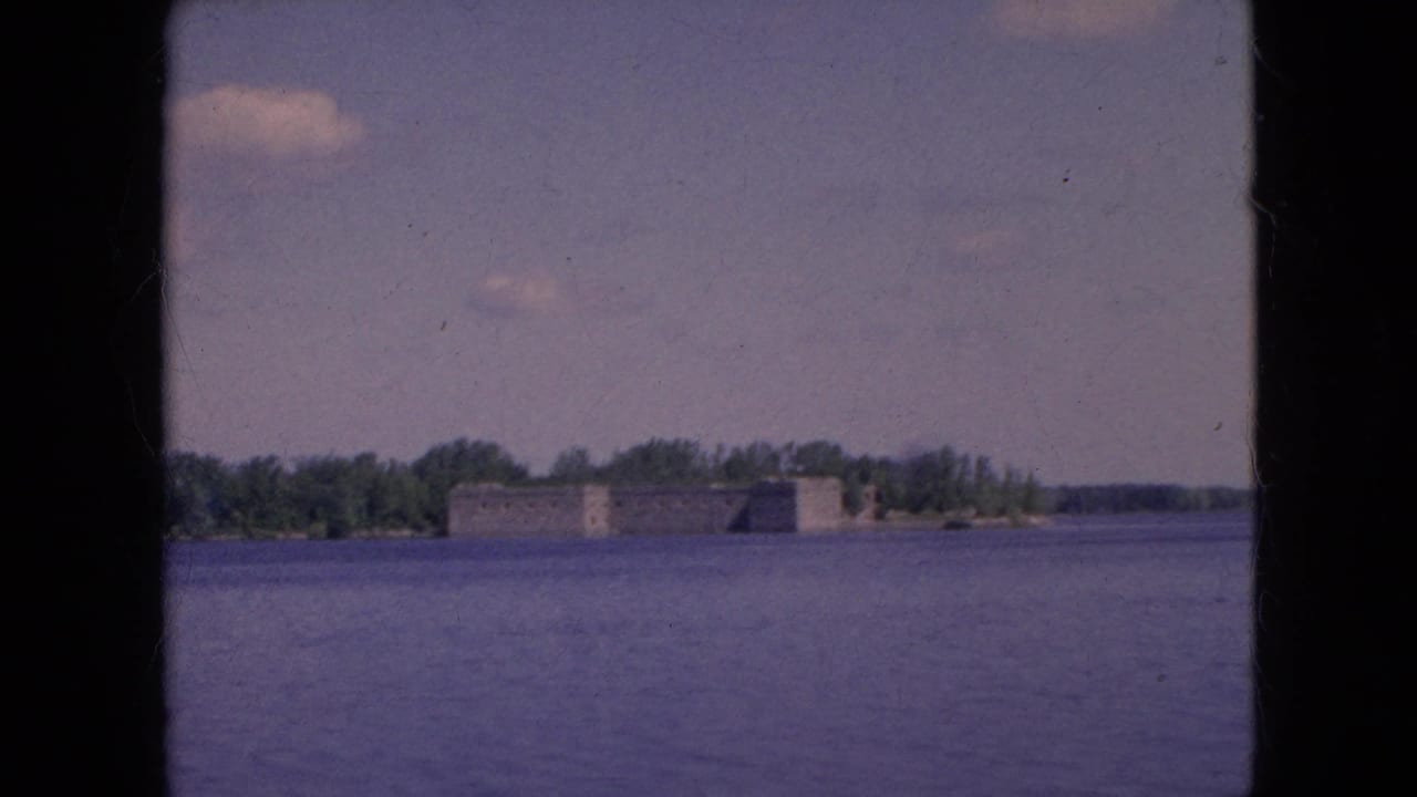 1964 Niagara Falls, New York home-movie frame showing a stone fort-like structure across broad water with trees along the far shore.