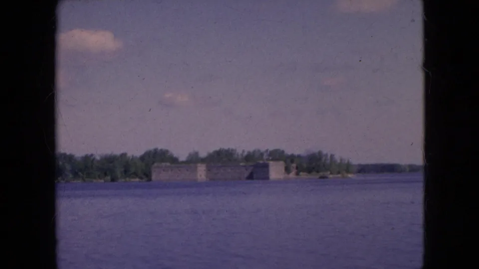 1964 Niagara Falls, New York home-movie frame showing a stone fort-like structure across broad water with trees along the far shore.