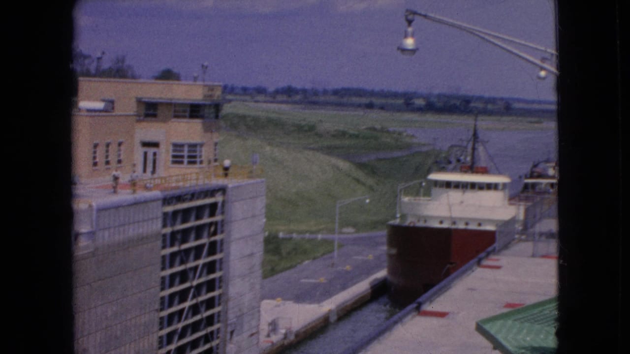 Freighter alongside the lock wall near a tan building and open water.