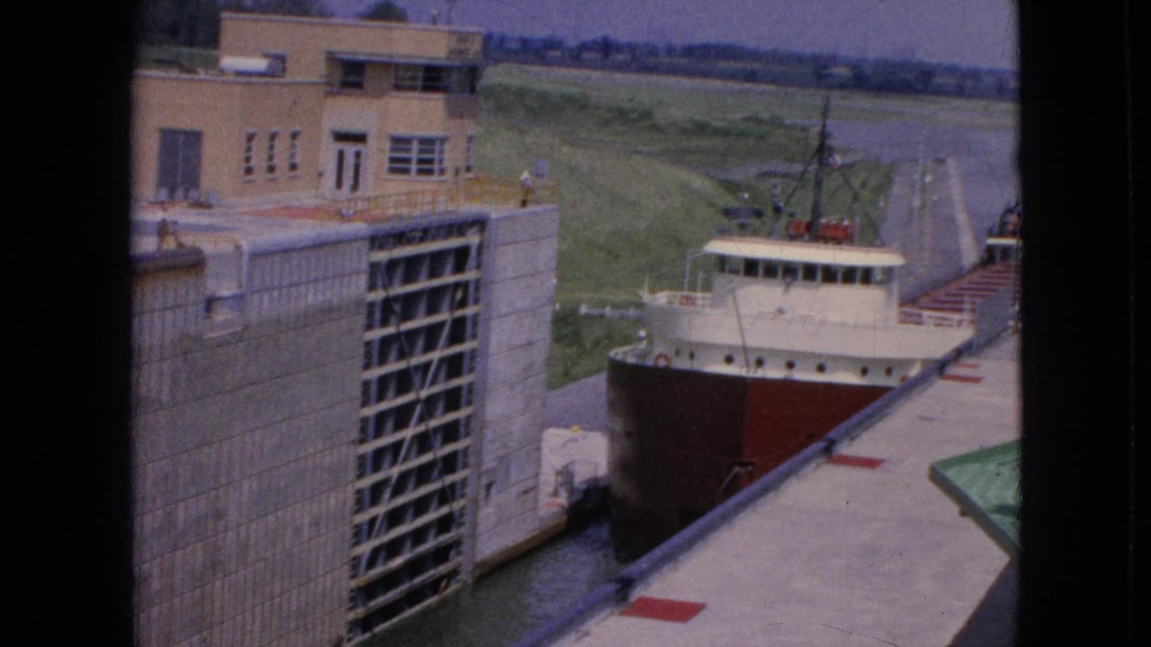1964 8mm frame of a large freighter with a red hull moving into a concrete lock at the Niagara Falls, New York location identified in the metadata.