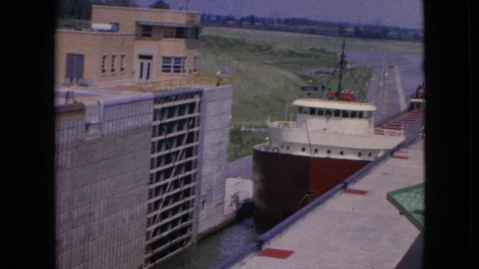 1964 8mm frame of a large freighter with a red hull moving into a concrete lock at the Niagara Falls, New York location identified in the metadata.