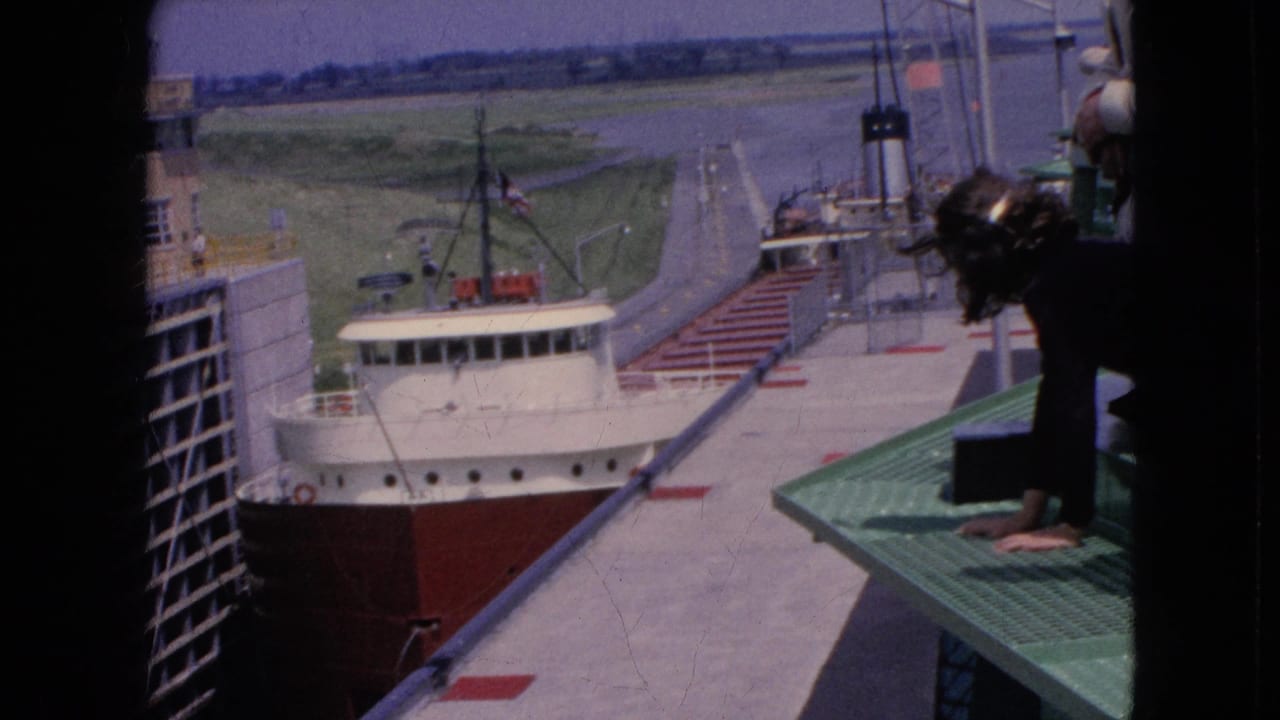 1964 Niagara Falls, New York frame of a freighter passing through a lock channel while a person leans over a green grated platform in the foreground.