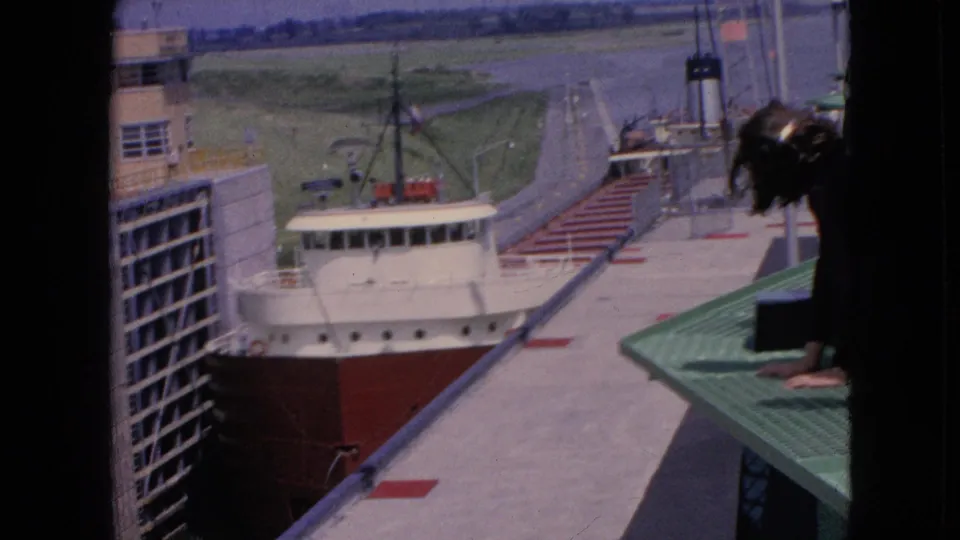 1964 Niagara Falls, New York 8mm frame showing the freighter lower in the lock channel as an observer leans over the green platform at the right edge.
