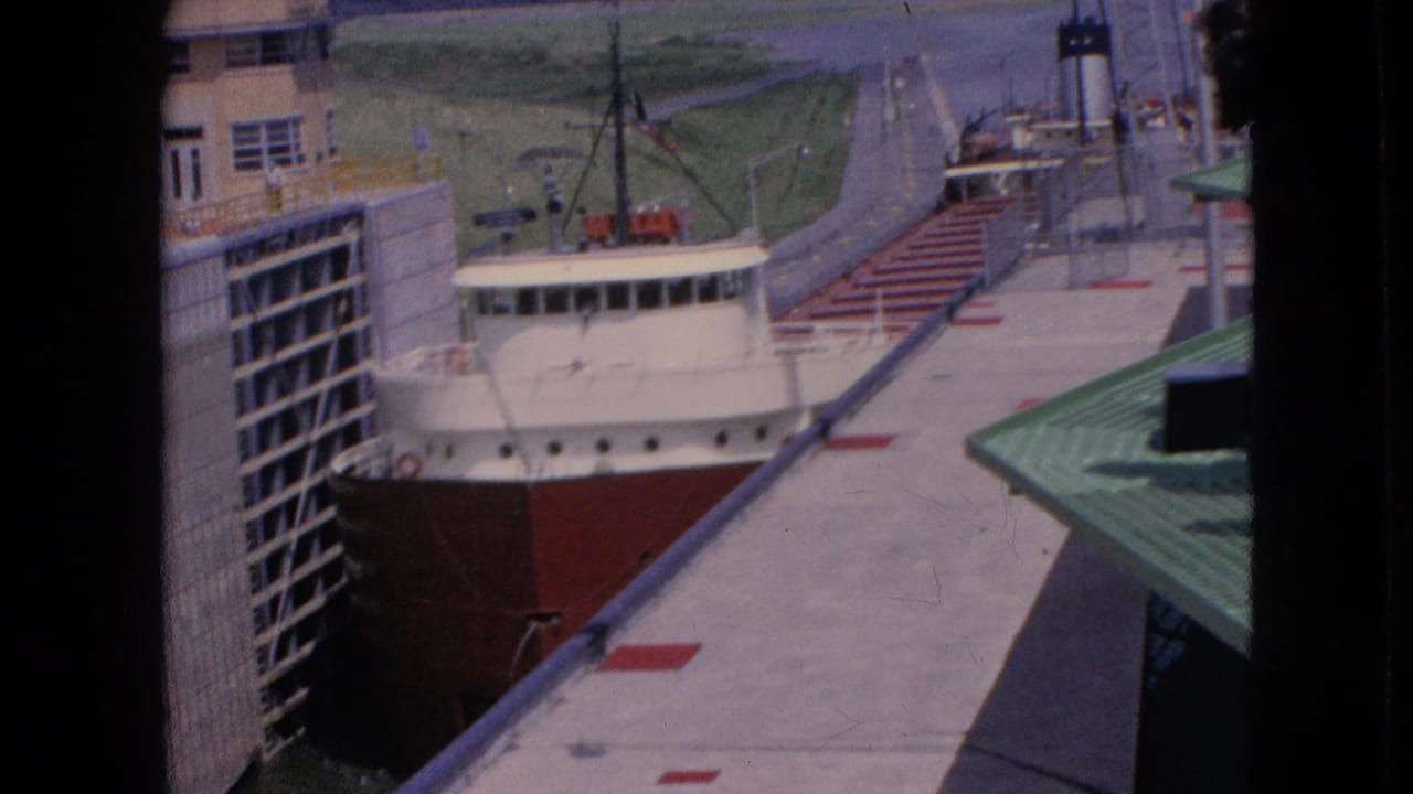 1964 8mm view at Niagara Falls, New York, showing a red-and-white freighter positioned in a concrete lock chamber beneath an elevated visitor viewpoint.