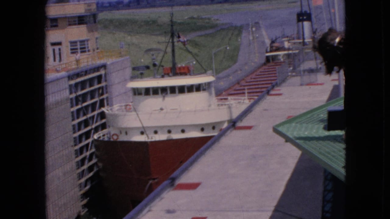 Red-and-white freighter sits alongside lock walls with dock and building visible above.