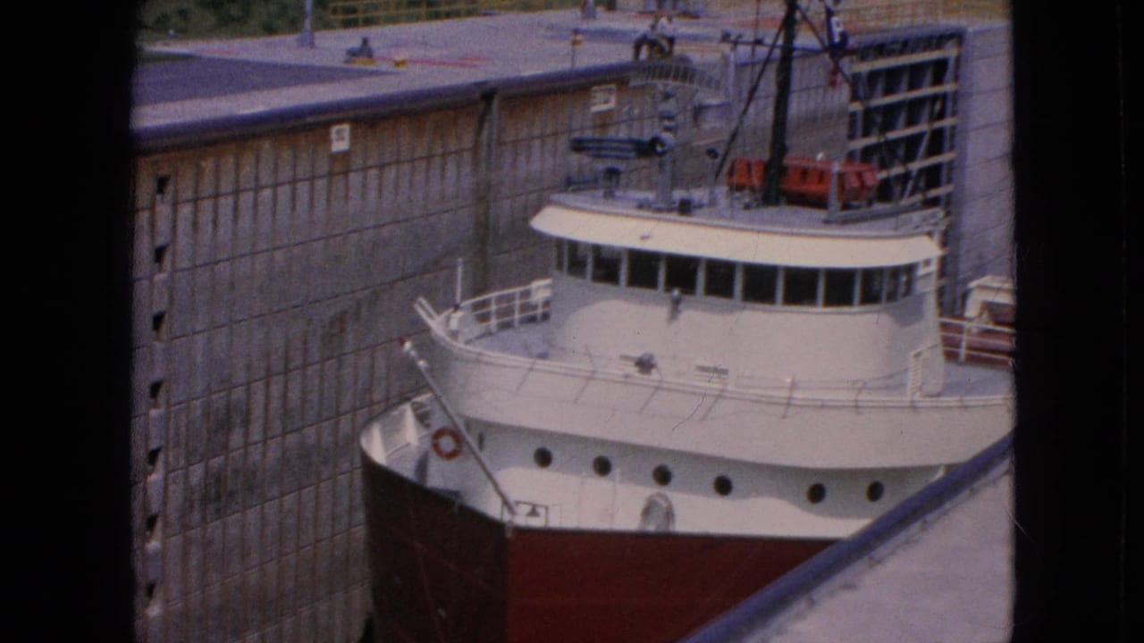 1964 8mm frame from Niagara Falls, New York showing the bow and wheelhouse of a white and red freighter beside tall concrete lock walls.
