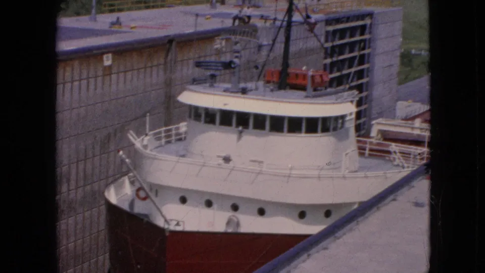 The vessel's white wheelhouse, red bow, railings, and deck equipment are seen close to the massive lock wall in this 1964 Niagara Falls home-movie frame.