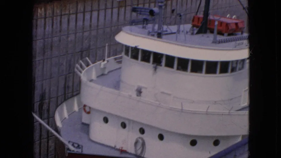 The freighter's bridge, bow railings, and portholes fill the frame as the vessel sits tightly within the Niagara Falls lock chamber in 1964 home-movie footage.