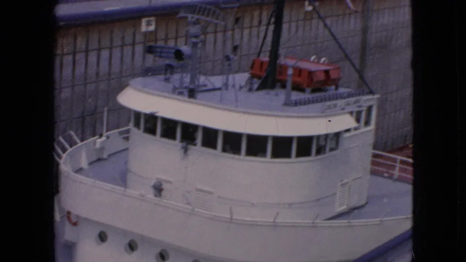 1964 8mm frame of the freighter's bridge and upper deck, with red lifeboats and railings visible as the ship remains close to the concrete lock wall.