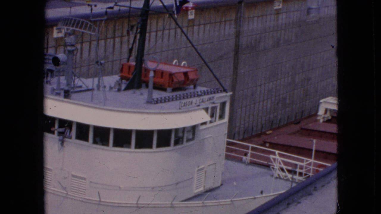 The white freighter's bridge and upper deck appear close to the tall concrete lock wall, with rigging, railings, and red deck equipment visible in the 1964 home-movie frame.