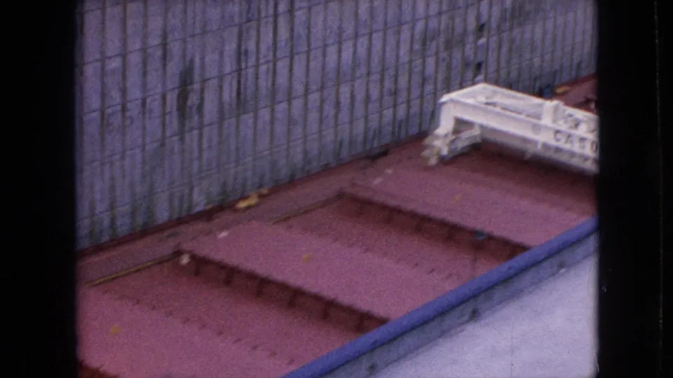 Overhead 1964 8mm frame showing red cargo hatches, a gray canal wall, and partial deck equipment from the Cason J. Callaway sequence.