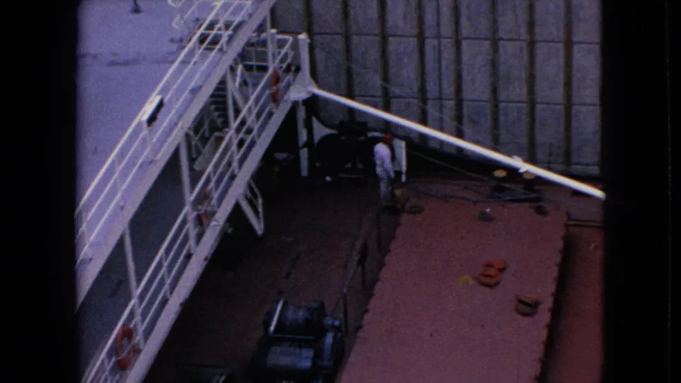 1964 8mm overhead frame from the Niagara Falls, New York canal footage showing ship railings, crane structure, deck gear, and a worker near the wall.