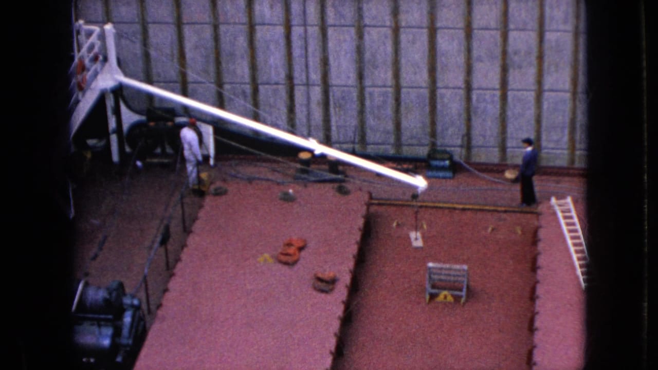 Red vessel deck with a long white boom, two people, a ladder, and industrial lock walls.