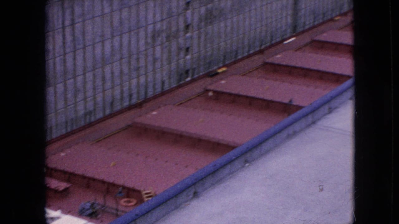 1964 Niagara Falls power facility view showing a gray concrete wall, red-painted metal deck panels, and a blue-gray railing or pipe from an elevated home-movie angle.